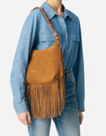 Petit sac hobo Jess noisette en cuir souple avec franges et bandoulière tressée, porté à l'épaule.
