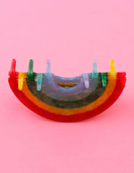 Gros plan sur la Pince à cheveux crabe de taille moyenne de la marque Coucou Suzette en acétate de cellulose brillant. L'accessoire prend la forme d'un arc-en-ciel incurvé aux bandes colorées et nacrées dans les tons rouge, jaune, vert, bleu et violet.