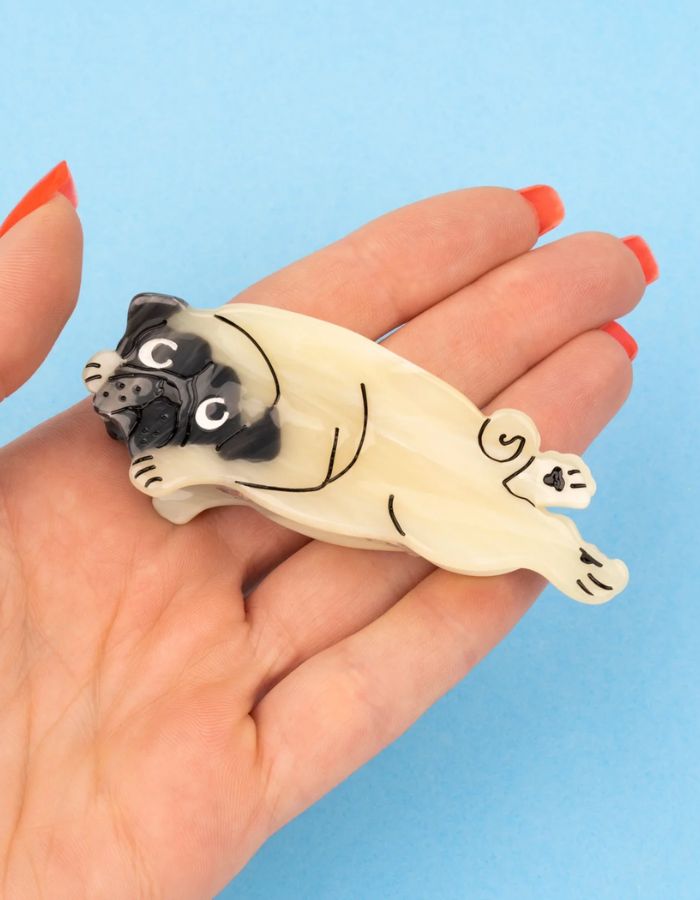 Gros plan sur la Pince à cheveux crabe de taille moyenne de la marque Coucou Suzette en acétate de cellulose beige brillant. L'accessoire représente un chien carlin rigolo de profil avec son museau noir plissé et ses petits yeux expressifs.