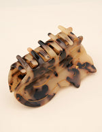 Gros plan sur la Pince à cheveux crabe de taille moyenne de la marque Coucou Suzette en acétate de cellulose brillant. L'accessoire représente un chat de gouttière de profil avec un pelage tacheté marron et noir style écaille de tortue et des détails dorés.