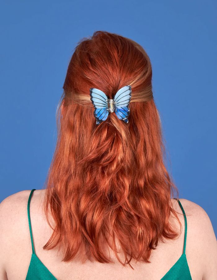 Mise en situation de la Pince à cheveux crabe de taille moyenne de la marque Coucou Suzette en acétate de cellulose brillant. L'accessoire prend la forme d'un papillon bleu azur et blanc nacré aux ailes déployées avec des contours noirs.