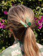 Mise en situation de la Pince à cheveux crabe de taille moyenne de la marque Coucou Suzette en acétate de cellulose brillant. L'accessoire prend la forme d'un papillon vert émeraude et vert menthe nacré aux ailes déployées avec des contours graphiques noirs