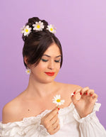 Jeune femme portant des pinces à cheveux pâquerette blanches et jaunes en acétate, assorties à ses boucles d'oreilles.