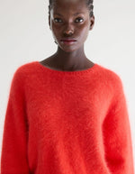 Femme portant un pull DIME Angora Salsa rouge intense, doux et duveteux, à col rond et coupe relaxed.