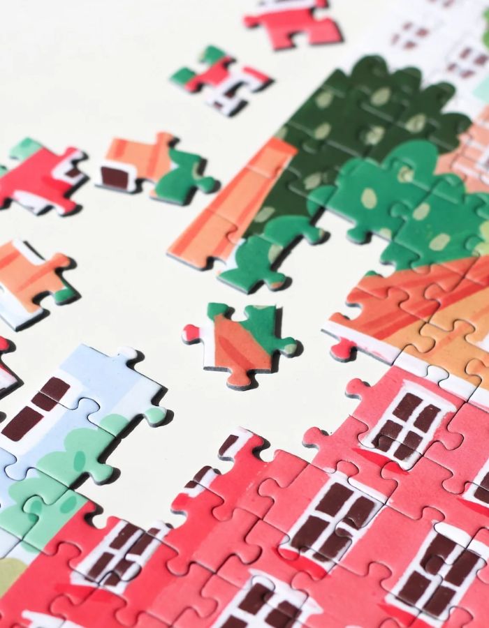 Gros plan sur le Puzzle de 1000 pièces pour adulte illustré par Serena White pour Piecely, représentant les canaux et les façades colorées de Copenhague au crépuscule. Présenté à côté de sa boîte de rangement élégante et écoresponsable.