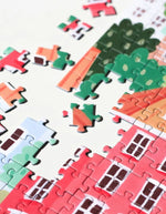 Gros plan sur le Puzzle de 1000 pièces pour adulte illustré par Serena White pour Piecely, représentant les canaux et les façades colorées de Copenhague au crépuscule. Présenté à côté de sa boîte de rangement élégante et écoresponsable.