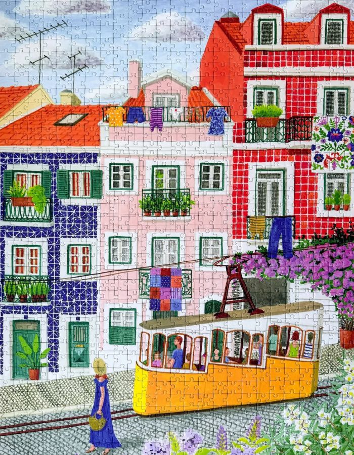 Puzzle de 1000 pièces pour adulte illustré par Mélanie Voituriez pour Piecely, représentant une rue colorée de Lisbonne avec le tramway jaune traditionnel et des façades en azulejos. Présenté aux côtés de sa boîte de rangement écoresponsable.