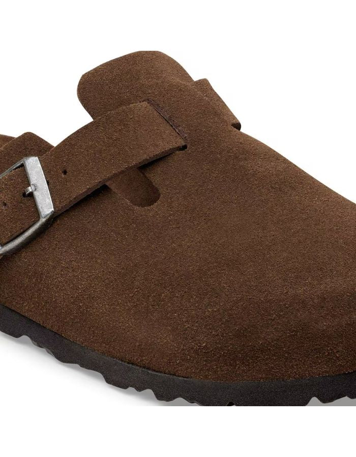 Boucle des Sabots fermés modèle Boston de la marque Birkenstock en cuir velours souple de couleur marron foncé Carafe. Présente une bride ajustable à boucle métallique sur le dessus et une semelle anatomique ton sur ton en liège avec lit de pied souple, version chaussant étroit.