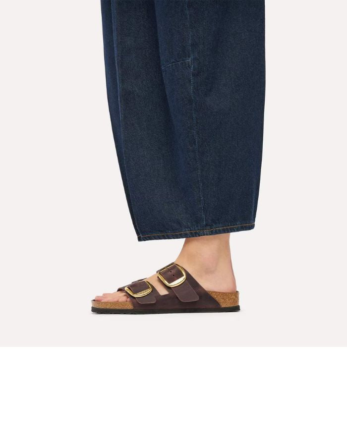 vue portée des Sandales Birkenstock modèle Arizona Big Buckle avec chaussant étroit. Présente deux larges brides en cuir huilé épais à bords bruts dotées de grandes boucles métalliques élégantes, montées sur la célèbre semelle anatomique en liège et cuir lisse assorti.