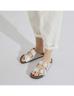 Vue portée des Sandales Birkenstock Arizona Big Buckle en largeur étroite. Les deux brides réglables sont en Birko-Flor® blanc nacré satiné (Graceful Pearl White) avec de grandes boucles en métal argenté, reposant sur une semelle anatomique en liège et cuir velours.
