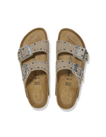 Sandales Birkenstock Arizona Rivets en cuir velours taupe avec deux brides réglables et boucles métalliques.