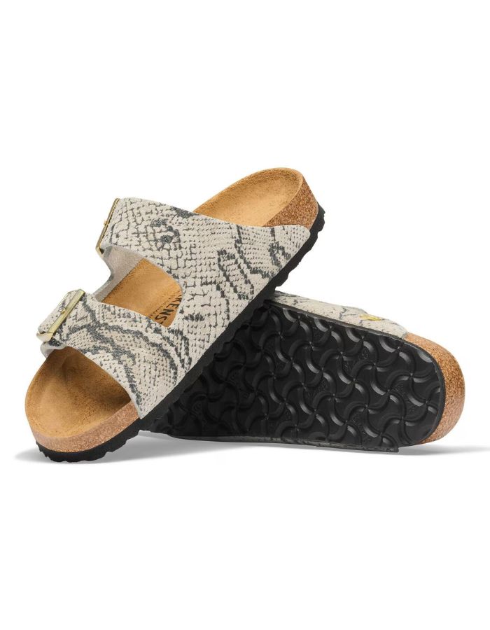 Semelle des Sandales pour pieds fins en largeur Narrow, modèle emblématique Arizona Rivet Logo de la marque Birkenstock. Confectionnées en cuir velours souple de couleur claire beige huître Snake Oyster, elles présentent deux brides horizontales ajustables avec boucles en métal, un rivet logo et la célèbre semelle anatomique marron en liège naturel