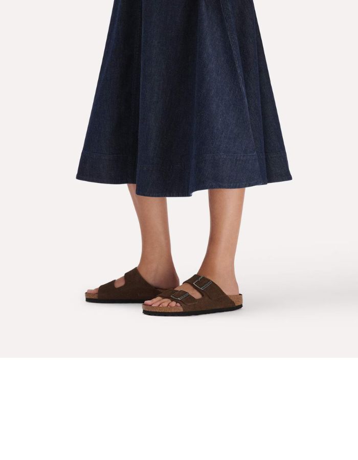 Vue de profil des Sandales Birkenstock modèle Arizona avec chaussant étroit. Présente deux brides ajustables en cuir velours souple de couleur marron foncé Carafe avec des boucles en métal assorties, montées sur la célèbre semelle anatomique en liège avec lit de pied souple.