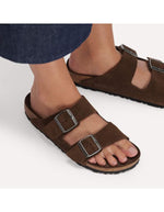 Dessus des Sandales Birkenstock modèle Arizona avec chaussant étroit. Présente deux brides ajustables en cuir velours souple de couleur marron foncé Carafe avec des boucles en métal assorties, montées sur la célèbre semelle anatomique en liège avec lit de pied souple.