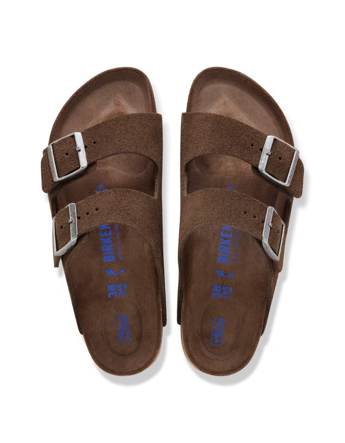 Dessus des Sandales Birkenstock modèle Arizona avec chaussant étroit. Présente deux brides ajustables en cuir velours souple de couleur marron foncé Carafe avec des boucles en métal assorties, montées sur la célèbre semelle anatomique en liège avec lit de pied souple.