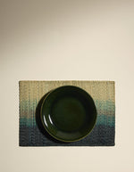 assiette sur un Set de table rectangulaire Orée Forêt par Maison Sarah Lavoine. Tressage artisanal en fibres naturelles de Carex avec dégradé vert forêt évoquant des silhouettes d'arbres, 45 x 30 cm