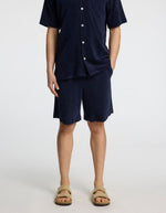 Homme portant un short et une chemise en tissu éponge bleu marine, avec des sandales beiges.