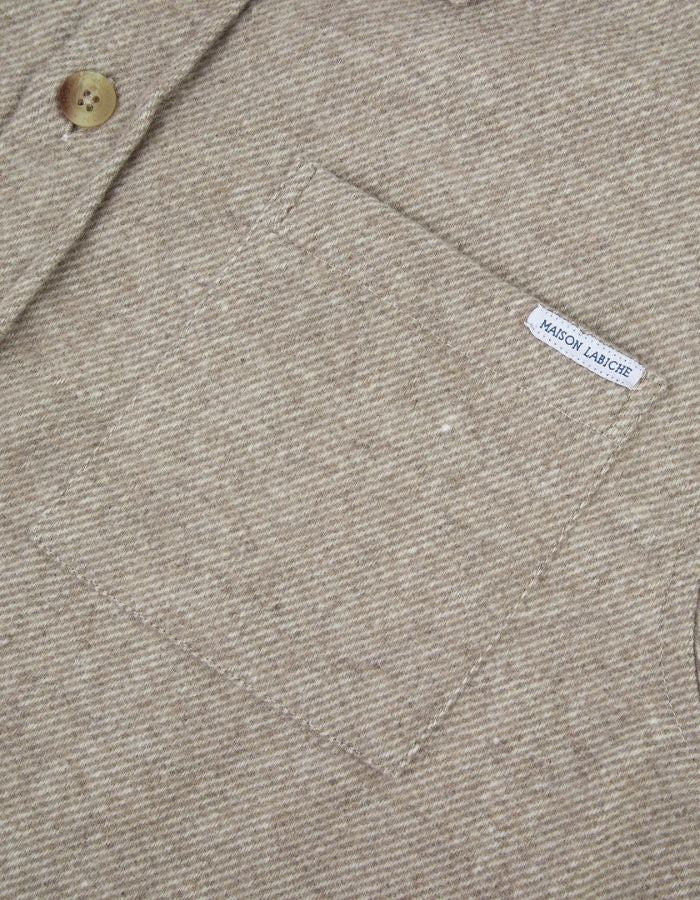 Poche de la Surchemise ample en flanelle de laine mélangée gris ciment pour homme, modèle Monge de la marque Maison Labiche. Présente une coupe droite large avec col chemise, fermeture boutonnée et deux poches plaquées sur la poitrine.