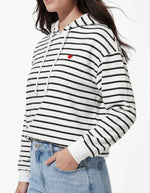 Gros plan sur le Sweatshirt à capuche pour femme modèle Chilli de la marque Pieces. Tissu blanc cassé Cloud Dancer à rayures horizontales noires, avec des emmanchures basses et une petite broderie en forme de cœur sur la poitrine.