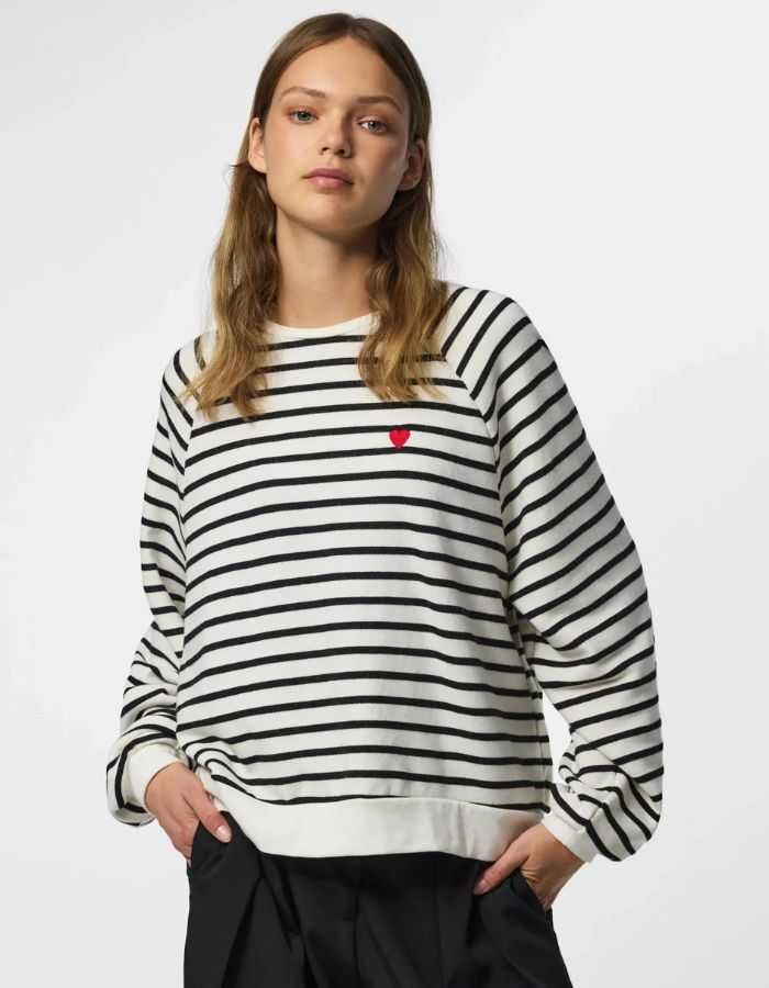 Vue de face du Sweatshirt à col rond et manches longues pour femme de couleur écru blanc cassé Cloud Dancer, modèle Greta de la marque PIECES. Présente une coupe classique droite avec un petit cœur noir brodé sur le côté gauche de la poitrine.