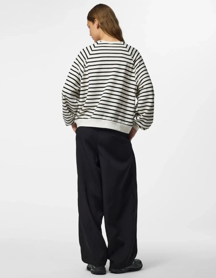 Silhouette de dos avec le Sweatshirt à col rond et manches longues pour femme de couleur écru blanc cassé Cloud Dancer, modèle Greta de la marque PIECES. Présente une coupe classique droite avec un petit cœur noir brodé sur le côté gauche de la poitrine.