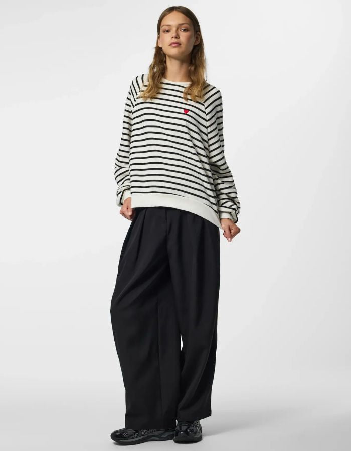 Silhouette avec le Sweatshirt à col rond et manches longues pour femme de couleur écru blanc cassé Cloud Dancer, modèle Greta de la marque PIECES. Présente une coupe classique droite avec un petit cœur noir brodé sur le côté gauche de la poitrine.