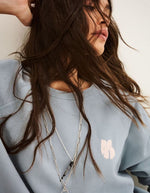 Col du Sweat-shirt pour femme en molleton doux de couleur bleu glacier pastel, modèle Swing de la marque Ba&sh. Présente une coupe ample loose avec col rond et manches raglan, rehaussée de surpiqûres overlock et d'une impression signature Ba&sh texturée sur la poitrine.