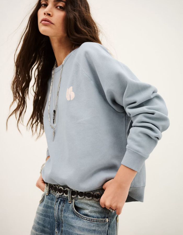 Manche du Sweat-shirt pour femme en molleton doux de couleur bleu glacier pastel, modèle Swing de la marque Ba&sh. Présente une coupe ample loose avec col rond et manches raglan, rehaussée de surpiqûres overlock et d'une impression signature Ba&sh texturée sur la poitrine.