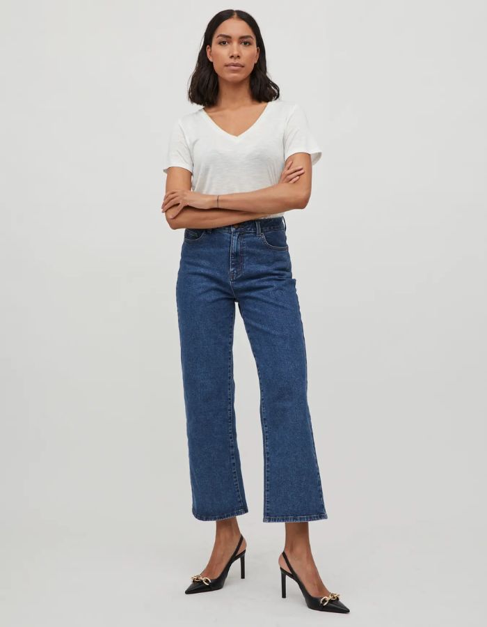 Femme portant un t-shirt blanc col V en jersey et un jean bleu foncé, avec des escarpins noirs.