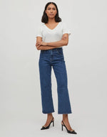 Femme portant un t-shirt blanc col V en jersey et un jean bleu foncé, avec des escarpins noirs.