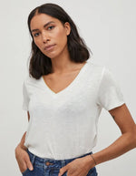 Femme portant un t-shirt blanc col V en jersey, avec un liseré doré subtil à l'encolure.