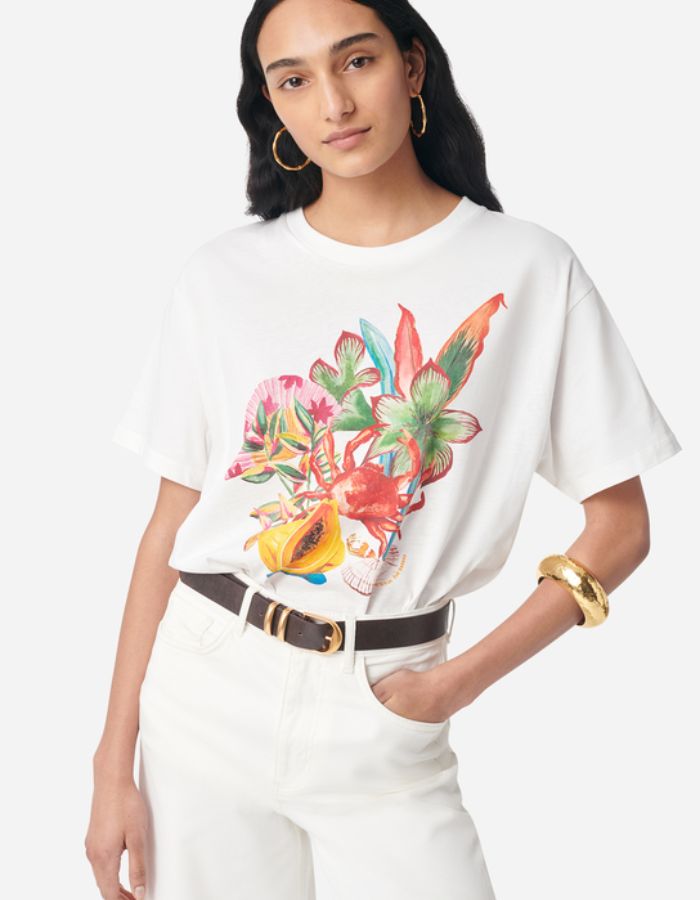 T-shirt Genesos blanc en coton organique avec imprimé floral, fruits et coquillages multicolores, porté par une femme.