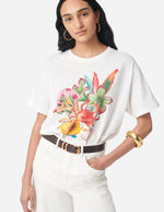 T-shirt Genesos blanc en coton organique avec imprimé floral, fruits et coquillages multicolores, porté par une femme.