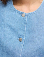 Détail du Top court en jean bleu clair Delila de ROUGE EDIT. Modèle à manches courtes bouffantes, encolure ronde et fermeture par boutons sur le devant. Coupe regular en coton denim.