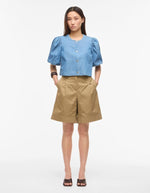 Silhouette avec le Top court en jean bleu clair Delila de ROUGE EDIT. Modèle à manches courtes bouffantes, encolure ronde et fermeture par boutons sur le devant. Coupe regular en coton denim.