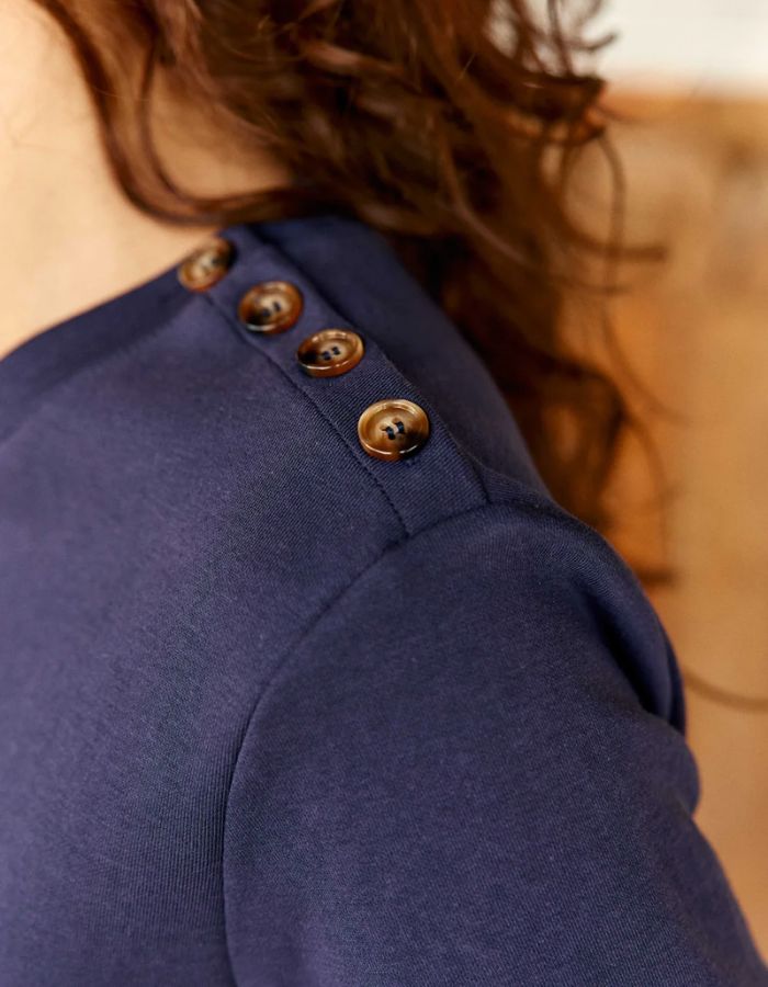 Vue de l'épaule du T-shirt bleu marine col rond pour femme en coton, modèle Taiga de la marque LA PETITE ÉTOILE. Présente une coupe droite à manches courtes et un boutonnage aspect corne sur l'épaule gauche.