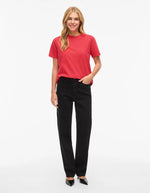 Femme souriante portant un t-shirt rouge uni à manches courtes et col rond, avec un jean noir.