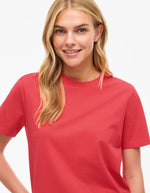 Femme souriante portant un t-shirt Nora Hibiscus rouge en jersey de coton biologique à manches courtes et col rond.