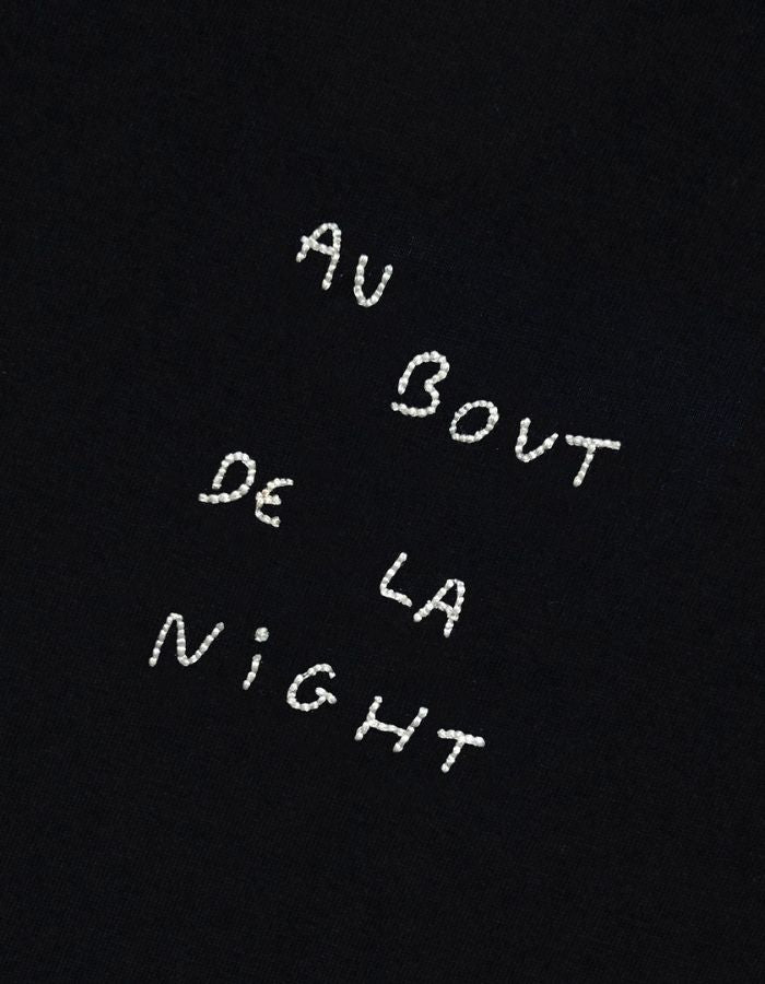 Broderie du T-shirt noir à manches courtes pour homme en coton biologique, modèle Popincourt de la marque Maison Labiche. Présente une coupe droite avec col rond en bord-côte et la phrase 'Au Bout De La Night' brodée en lettres fines sur le côté gauche de la poitrine.