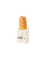 Vase Baguette en céramique doré, imitant une baguette dans un sac de boulangerie blanc.