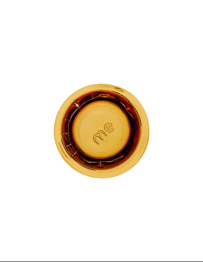 Vue sur le dessous du verre à eau artisanal Memento Dune couleur ambre, en pâte de verre soufflée à la bouche avec des ondulations naturelles et une forme pincée ergonomique.
