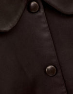 Boutonnière de la Veste courte pour femme en cuir d'agneau marron avec col claudine, manches mi-longues et boutons-pression recouverts, modèle Milos de la marque ba&sh.