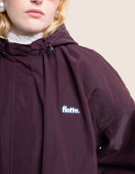 Logo sur la Veste imperméable oversize mixte violette cassis avec détails plissés, effet bouffant et capuche amovible, modèle Garance couleur Cassis de la marque Flotte.