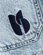 Logo brodé bleu marine sur la poche poitrine d'une veste en jean bleu clair délavé.