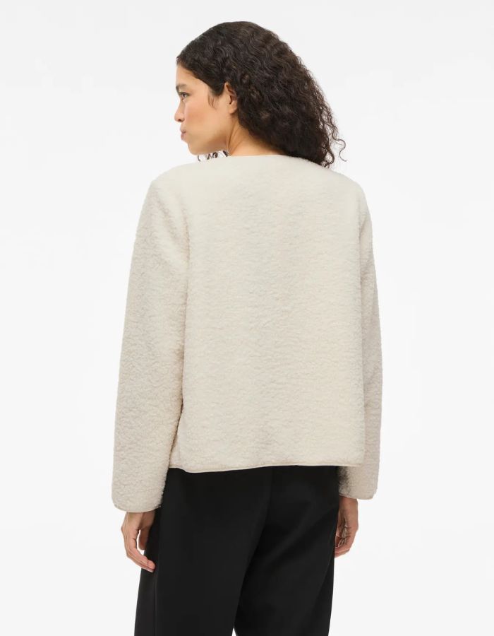 Silhouette de dos avec la Veste courte pour femme effet moumoute fausse fourrure de couleur beige écru, modèle Ada Teddy Jacket de la marque VILA. Présente un col chemise rabattu, des manches longues et une fermeture boutonnée sur le devant.