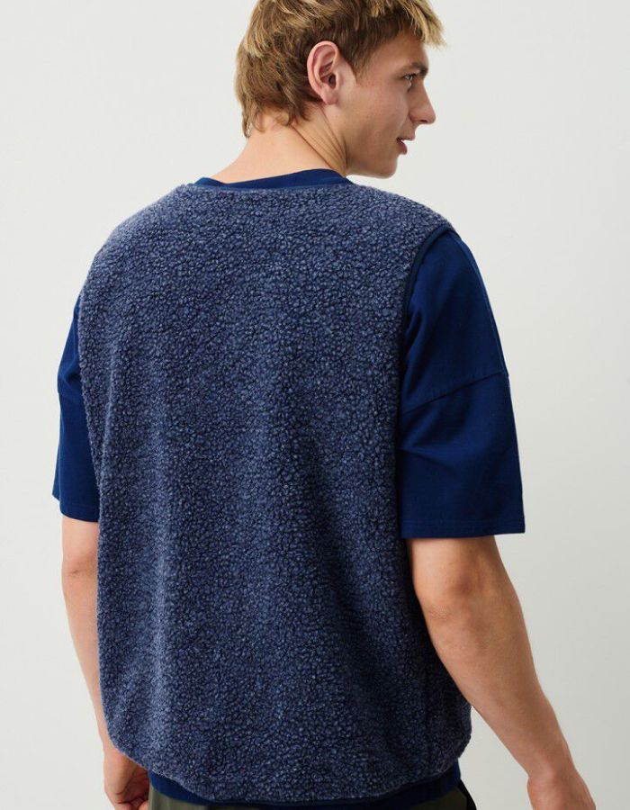 Dos de la Veste sans manches pour homme de couleur bleu nuit foncé Astre Chiné, modèle Hoktown de la marque American Vintage. Confectionnée dans une matière épaisse effet mouton retourné shearling, elle présente un col montant bas, une fermeture à boutons-pression, deux poches zippées et un patch logo sur la poitrine.
