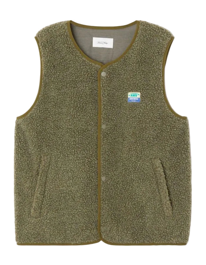 Veste sans manches pour homme de couleur vert kaki Varan Chiné, modèle Hoktown de la marque American Vintage. Confectionnée dans une matière épaisse effet mouton retourné shearling, elle présente un col montant bas, une fermeture à boutons-pression, deux poches zippées et un patch logo sur la poitrine.