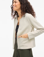 Femme souriante portant une veste beige zippée Garden Vila en maille côtelée, coupe courte, col rond et poches avant.