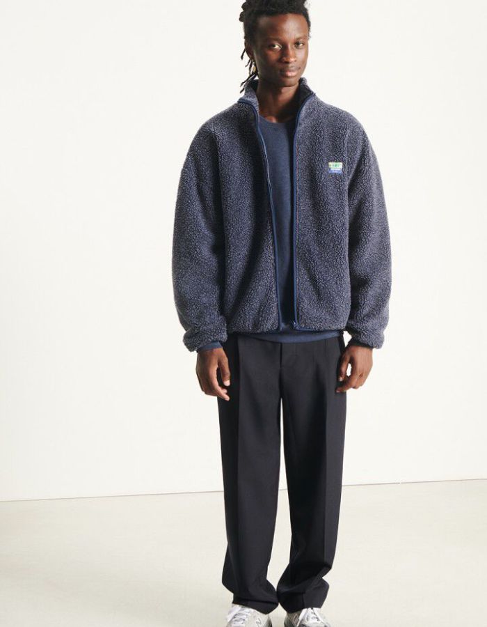 Silhouette avec la Veste zippée à manches longues pour homme de couleur bleu nuit foncé Astre Chiné, modèle Hoktown de la marque American Vintage. Confectionnée dans une matière épaisse effet mouton retourné shearling, elle présente un col montant bas, une fermeture éclair, deux poches zippées et un écusson logo AMV sur la poitrine.