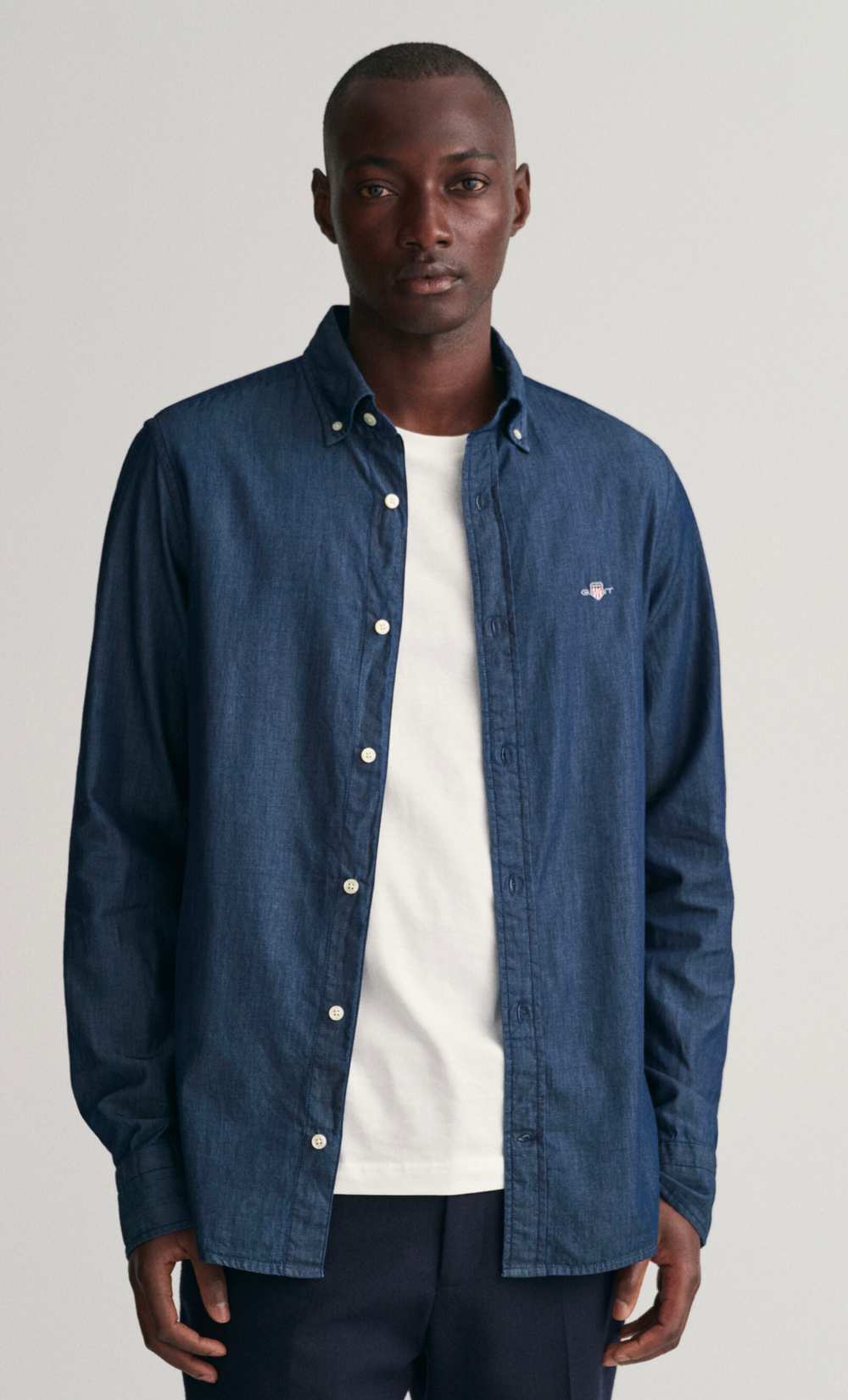 Homme portant une chemise slim fit indigo en chambray de coton avec col boutonné et écusson Gant.